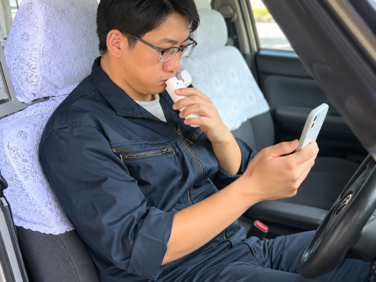 車内でアルコール検知器へ息を吹き込む運転者